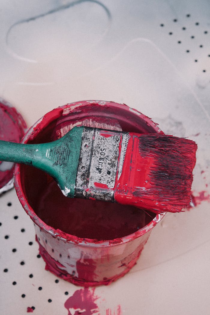 Close-up of a paintbrush resting on a red paint can, ideal for DIY projects or home decor.