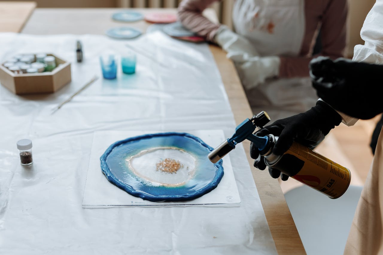 Close-up of hands using a gas burner to work on a resin art project at a desk.
